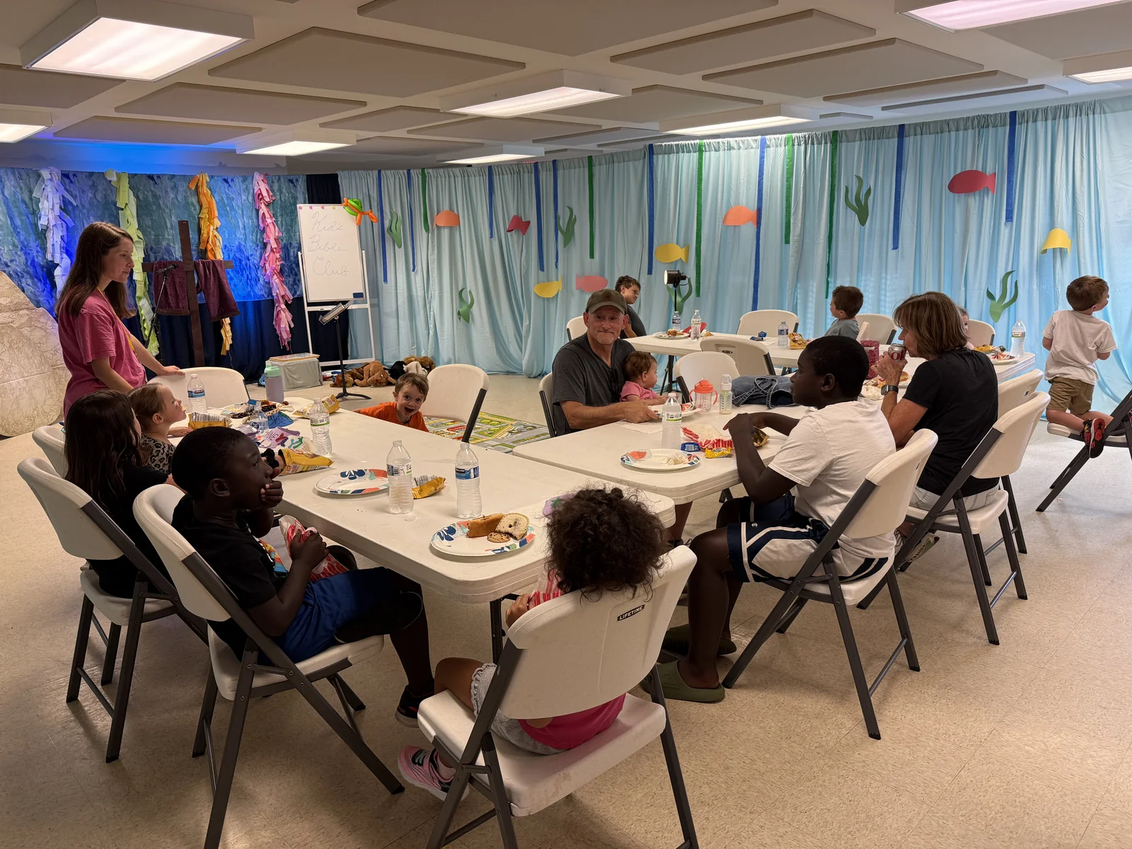 Children and adults gathered around tables during Backyard Bible Club.
