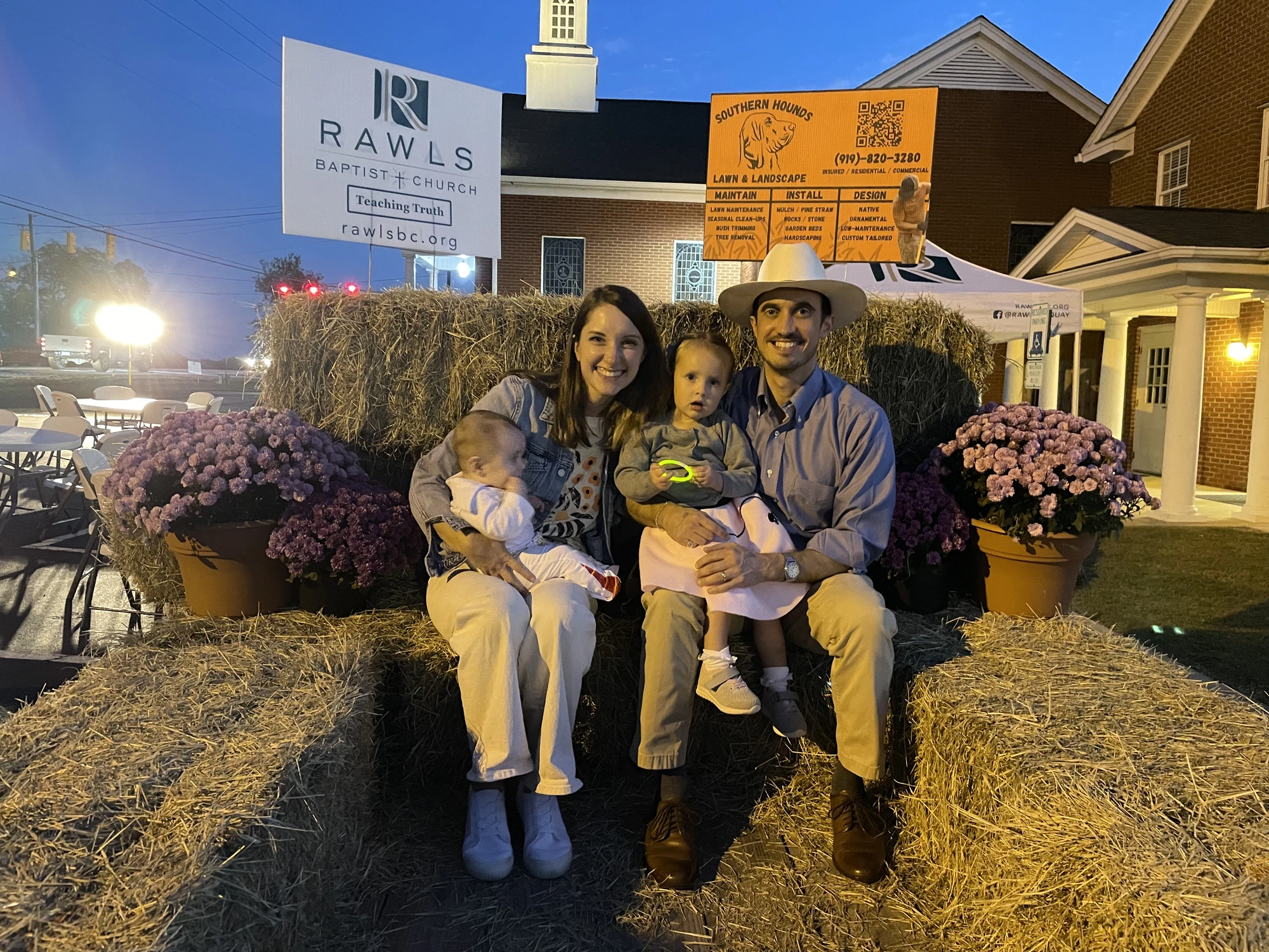 The pastor and his family seated together among hay bales and fall flowers at Trunk or Treat.