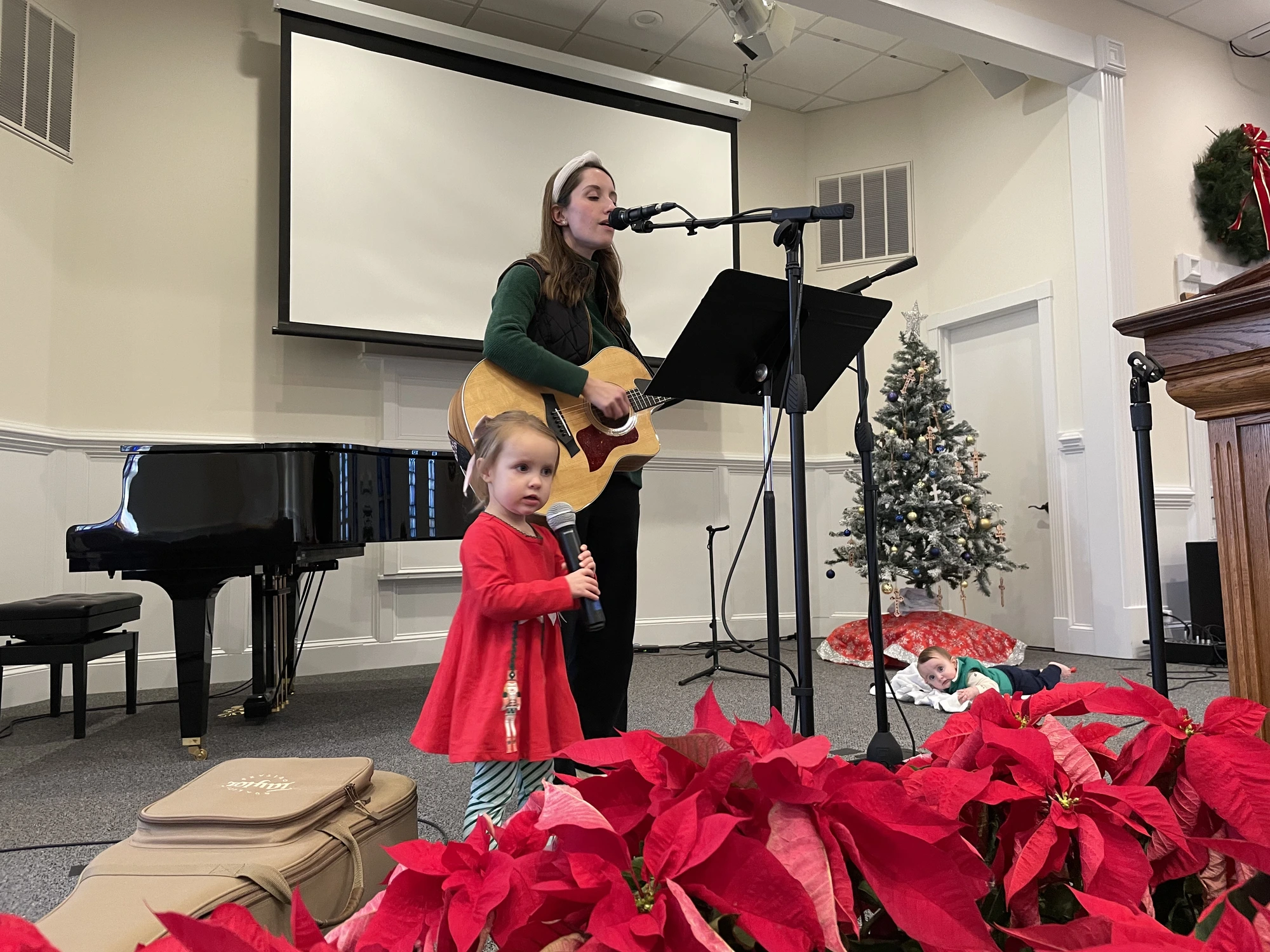 A mother playing guitar while her young daughter holds a microphone during Christmas worship.